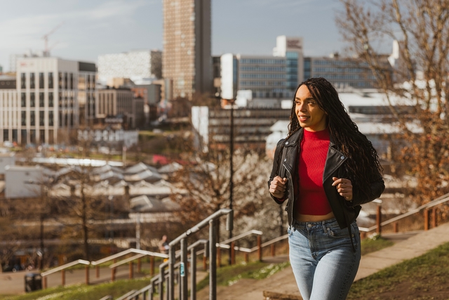 Smiling woman walking up steps behind station showing view across Sheffield