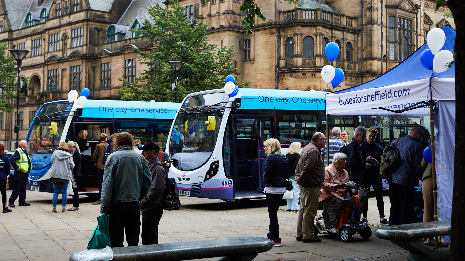 Busses surrounded with balloons and people like there's a celebration