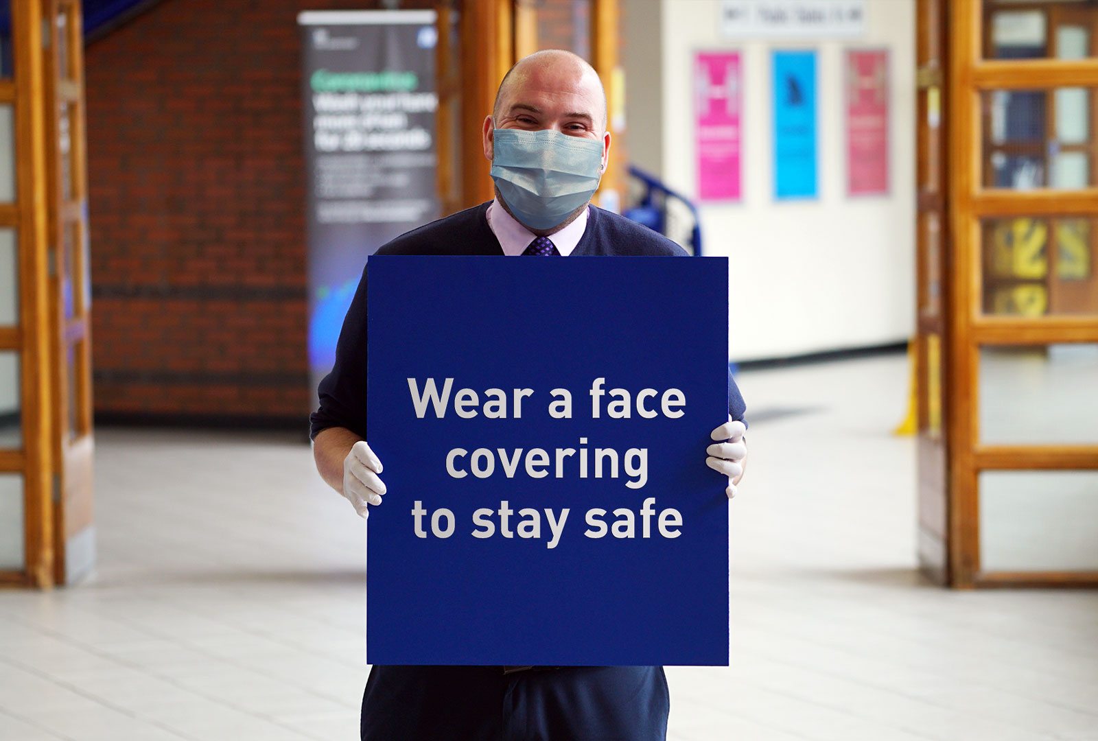 Man wearing mask holding sign saying 'Wear a face covering to stay safe'.