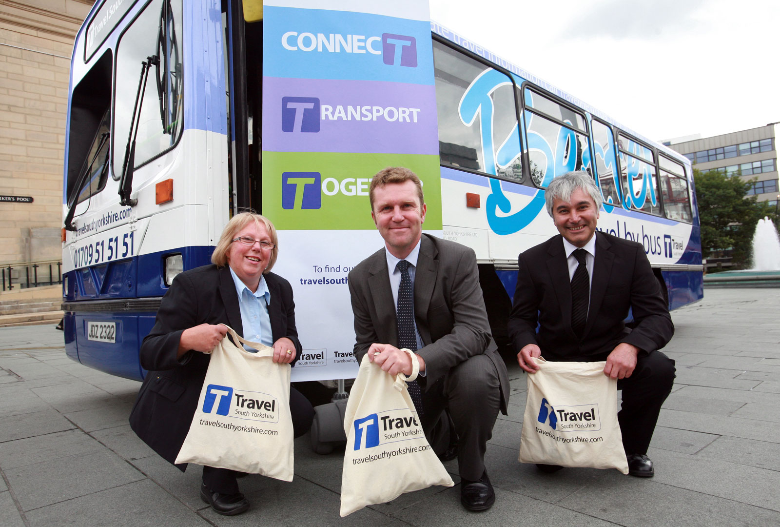 Three people showing new branded tote bags in front of new branded bus